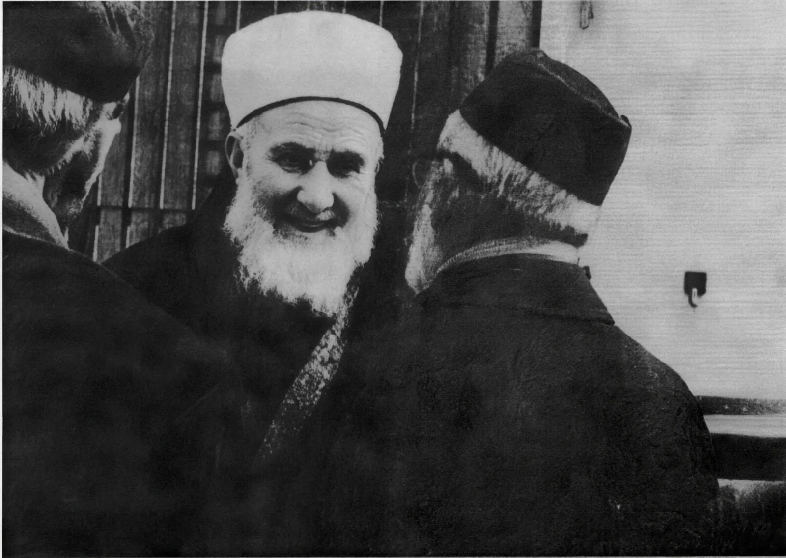 Mehmed Zahid Kotku smiling, between two men in conversation